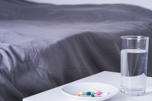 Close up pill drugs in the dish and a glass of water on nightstand in the bedroom. Healthcare and medical pharmacy concept
