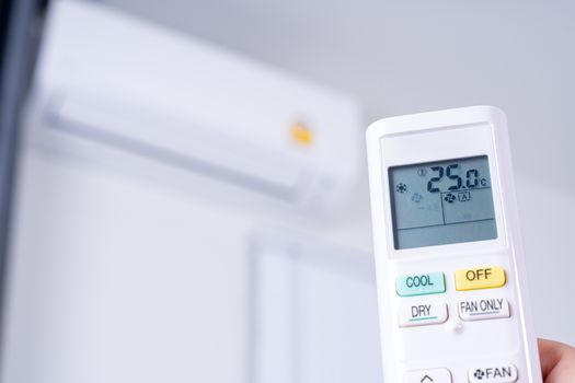 Human hand is using white remote of air conditioner for turn on or adjust temperature of air conditioner inside the room.