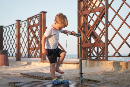 Child wash legs after beach sand Caucasian boy standing beach. Childhood summertime. Family vacation with one child.