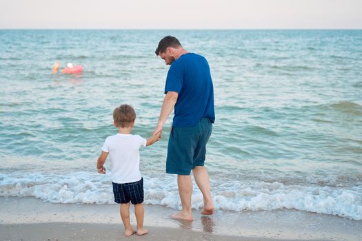 Dad holds son hand. Father Child spending time together sea vacation Young man little boy walking beach Fathers day. Family with one child. Happy childhood with daddy. Full lenght