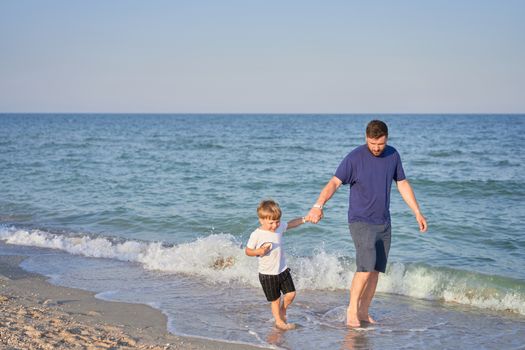 Dad holds son hand. Father Child spending time together sea vacation Young man little boy walking beach Fathers day. Family with one child. Happy childhood with daddy. Full lenght