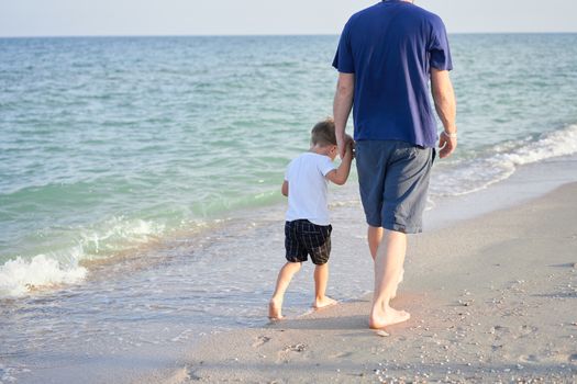 Dad holds son hand. Father Child spending time together sea vacation Young man little boy walking beach Fathers day. Family with one child. Happy childhood with daddy.