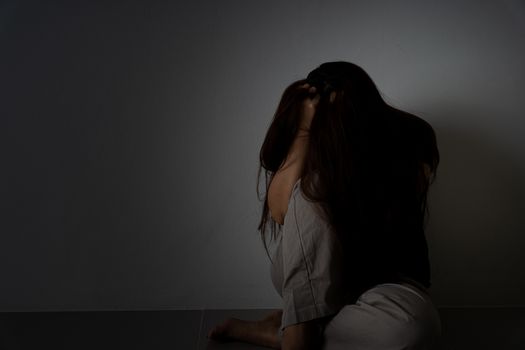 sad woman hug her knee and cry sitting alone in a dark room. Depression, unhappy, stressed and anxiety disorder concept.