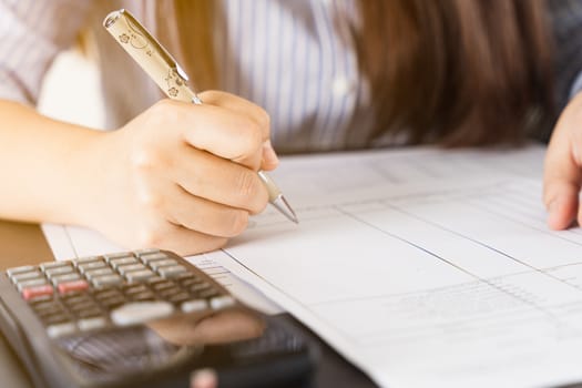 businesswoman working on desk office holding pen and using a calculator to calculate the numbers. Expenses, taxes, home budget finance accounting concept.