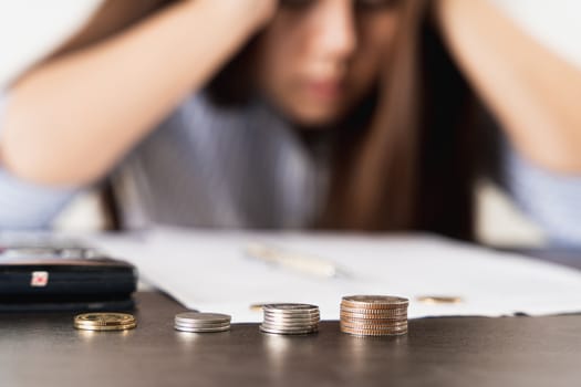 Close up coins on the desk with businesswoman working on desk office with depression, unhappy and stressed emotion. Expenses, taxes, home budget finance accounting concept.
