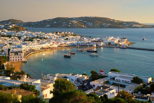 View of Mykonos town Greek tourist holiday vacation destination with famous windmills, and port with boats and yachtson sunset . Mykonos, Cyclades islands, Greece.