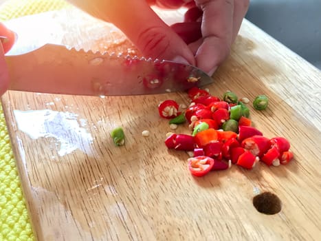 Close-up hand chopped the red chilli on a wooden cutting board, cooking at home concept.