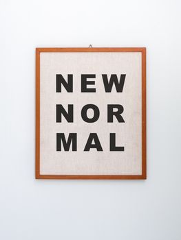 "New normal" word on light brown canvas on hanging wooden frame isolated on white background, vertical style.