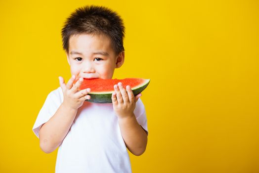 Happy portrait Asian child or kid cute little boy attractive laugh smile playing holds cut watermelon fresh for eating, studio shot isolated on yellow background, healthy food and summer concept