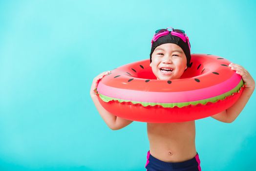 Summer vacation concept, Portrait Asian happy cute little child boy wear goggles and swimsuit hold watermelon inflatable ring, Kid having fun on summer vacation, studio shot isolated blue background