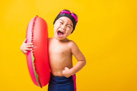 Summer vacation concept, Portrait Asian happy cute little child boy wear goggles and swimsuit hold watermelon inflatable ring, Kid having fun on summer vacation, studio shot isolated yellow background