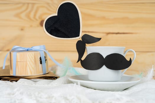 Happy Father Day background concept with and cup of tea, black mustache, black heart shape and gift box on wooden background with copy space for text.
