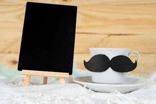 Happy Father Day background concept with and cup of tea, black mustache and blackboard on wooden background with copy space for text.