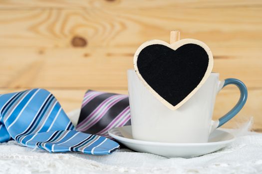Happy Father Day background concept with and cup of tea, black heart shape and blue and pink necktie on wooden background with copy space for text.