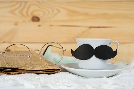 Happy Father Day background concept with and cup of tea, black mustache, glasses and newspaper on wooden background with copy space for text.