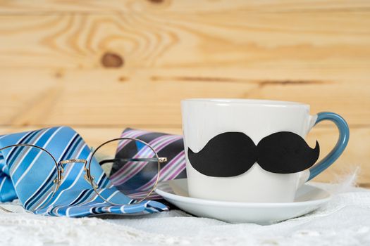 Happy Father Day background concept with and cup of tea, black mustache and blue and pink necktie on wooden background with copy space for text.