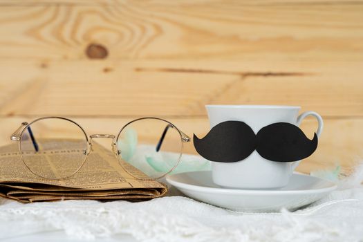 Happy Father Day background concept with and cup of tea, black mustache, glasses and newspaper on wooden background with copy space for text.