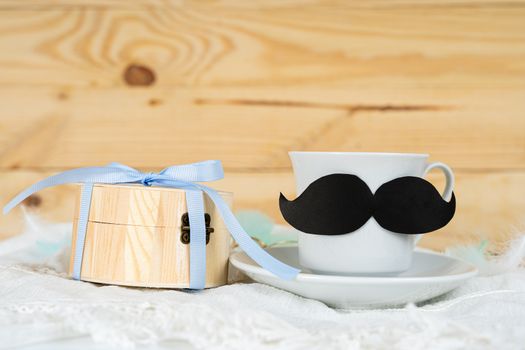Happy Father Day background concept with and cup of tea, black mustache and gift box on wooden background with copy space for text.