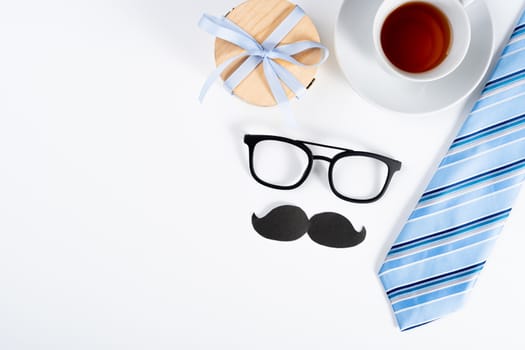 Happy Father Day background concept with blue necktie, black mustache, glasses, cup of tea and gift box on white background with copy space for text.