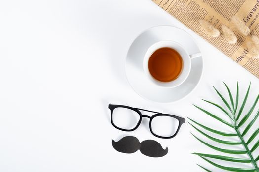 Happy Father Day background concept with newspaper, leaf, black mustache, glasses and cup of tea on white background with copy space for text.