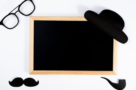 Happy Father Day background concept with blackboard and paper cut of hat, glasses, black mustache and smoking pipe on white background with copy space for text.