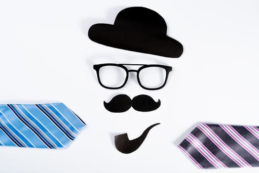 Happy Father Day background concept with blue and pink necktie and paper cut of hat, glasses, black mustache and smoking pipe on white background with copy space for text.