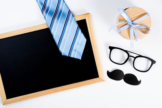 Happy Father Day background concept with blue necktie, glasses, cup of tea, gift box, black mustache and blackboard on white background with copy space for text.