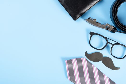 Happy Father Day background concept with pink necktie, glasses, wallet, belt and black mustache on blue background with copy space for text.
