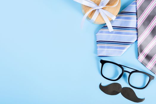 Happy Father Day background concept with blue necktie, glasses, gift box and black mustache on blue background with copy space for text.