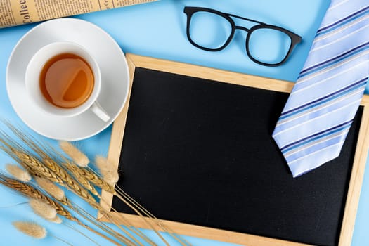 Happy Father Day background concept with blue necktie glasses, newspaper, dry grass flower, cup of tea and blackboard on blue background with copy space for text.