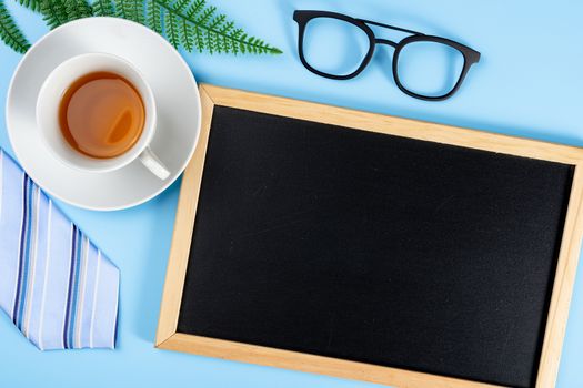 Happy Father Day background concept with blue necktie glasses, leaf, cup of tea and blackboard on blue background with copy space for text.