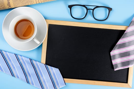 Happy Father Day background concept with blue and pink necktie glasses, newspaper, cup of tea and blackboard on blue background with copy space for text.