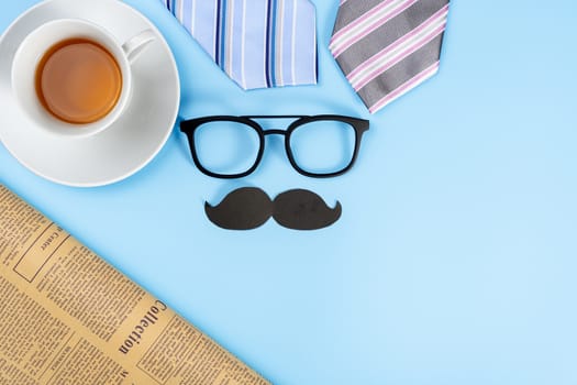 Happy Father Day background concept with blue and pink necktie, glasses, newspaper, cup of tea and black mustache on blue background with copy space for text.
