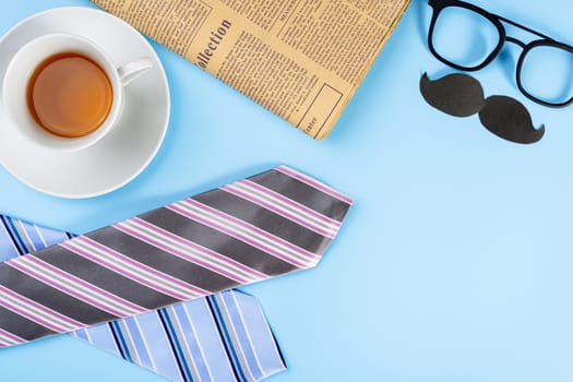 Happy Father Day background concept with blue and pink necktie, glasses, newspaper, cup of tea and black mustache on blue background with copy space for text.