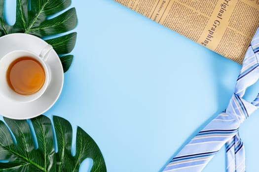Happy Father Day background concept with blue necktie, newspaper, leaf and cup of tea on blue background with copy space for text.