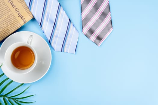 Happy Father Day background concept with blue and pink necktie, newspaper, leaf and cup of tea on blue background with copy space for text.