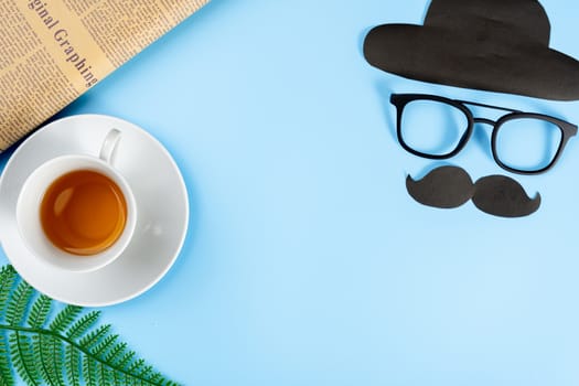 Happy Father Day background concept with glasses, black mustache, hat, newspaper, leaf and cup of tea on blue background with copy space for text.