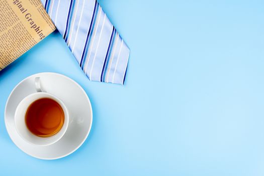 Happy Father Day background concept with blue necktie, newspaper and cup of tea on blue background with copy space for text.