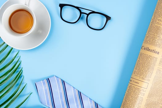Happy Father Day background concept with blue necktie, glasses, newspaper, leaf and cup of tea on blue background with copy space for text.