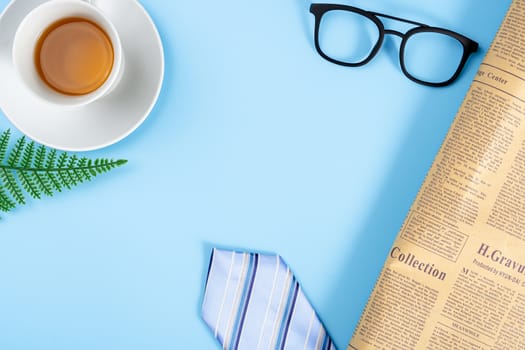 Happy Father Day background concept with blue necktie, glasses, newspaper, leaf and cup of tea on blue background with copy space for text.