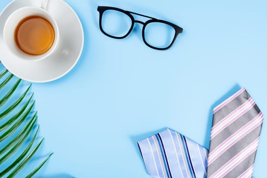 Happy Father Day background concept with blue and pink necktie, glasses, newspaper, leaf and cup of tea on blue background with copy space for text.