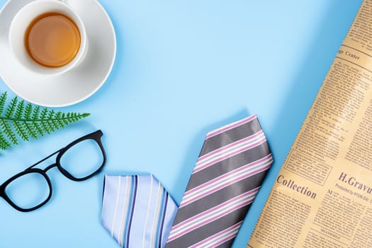 Happy Father Day background concept with blue and pink necktie, glasses, newspaper, leaf and cup of tea on blue background with copy space for text.