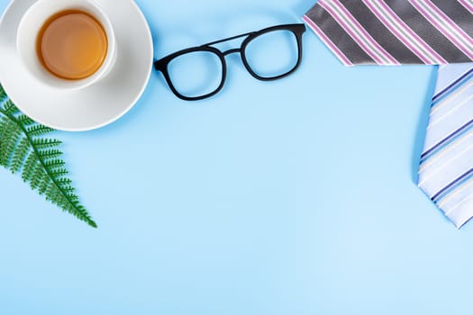 Happy Father Day background concept with pink necktie, glasses, newspaper, leaf and cup of tea on blue background with copy space for text.