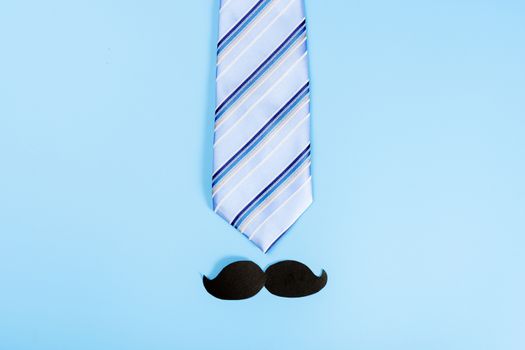 Happy Father Day background concept with blue necktie and black mustache on blue background with copy space for text.