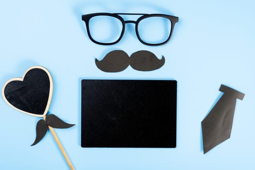 Happy Father Day background concept with glasses, blackboard, black heart shape, tie and black mustache on blue background with copy space for text.