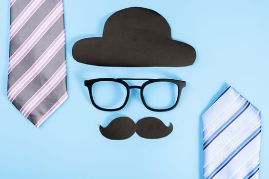 Happy Father Day background concept with blue and pink necktie, glasses, black hat and black mustache on blue background with copy space for text.