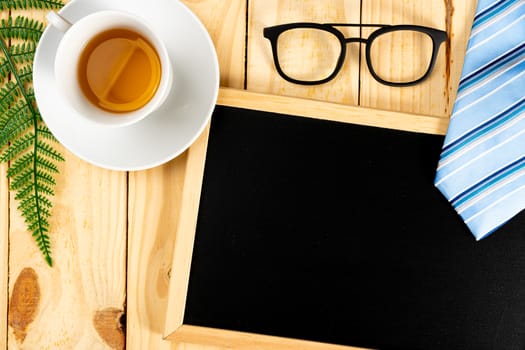 Happy Father Day background concept with blue necktie, glasses, cup of tea and blackboard on wooden background with copy space for text.