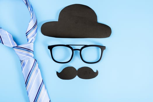 Happy Father Day background concept with blue necktie, glasses, black hat and black mustache on blue background with copy space for text.