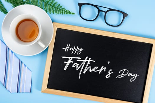 Happy Father Day background concept with blue necktie glasses, leaf, cup of tea and blackboard on blue background with copy space for text.