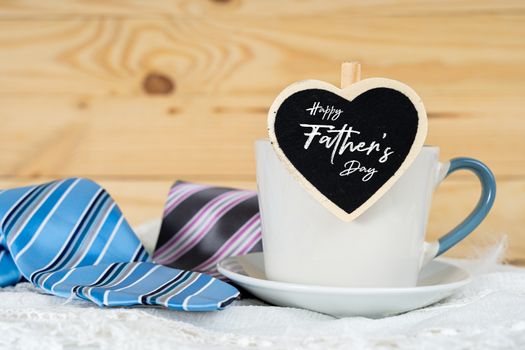 Happy Father Day background concept with and cup of tea, black heart shape and blue and pink necktie on wooden background with copy space for text.